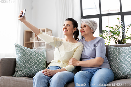 Image of senior mother with daughter taking selfie at home