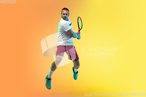 Image of Caucasian male professional sportsman playing tennis on studio background in neon light