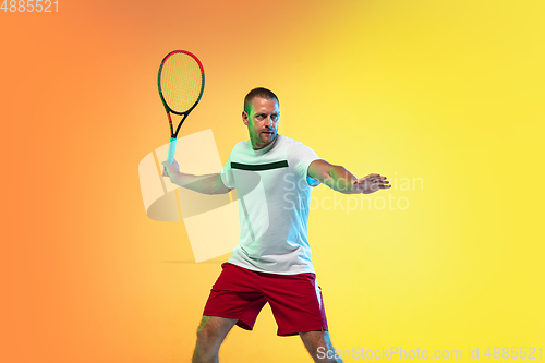 Image of Caucasian male professional sportsman playing tennis on studio background in neon light