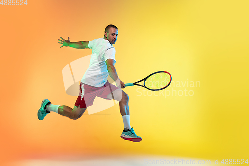 Image of Caucasian male professional sportsman playing tennis on studio background in neon light