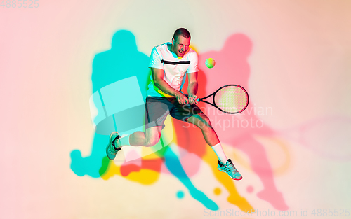 Image of Caucasian male professional sportsman playing tennis on studio background in neon light