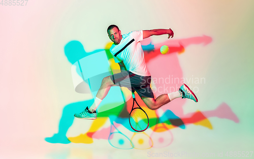 Image of Caucasian male professional sportsman playing tennis on studio background in neon light