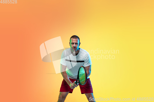 Image of Caucasian male professional sportsman playing tennis on studio background in neon light