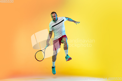 Image of Caucasian male professional sportsman playing tennis on studio background in neon light