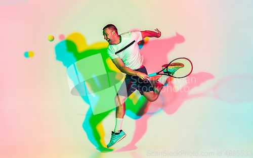 Image of Caucasian male professional sportsman playing tennis on studio background in neon light