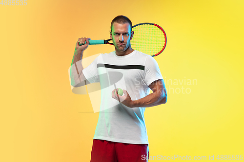 Image of Caucasian male professional sportsman playing tennis on studio background in neon light