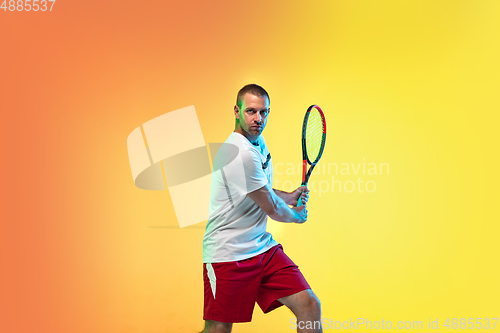 Image of Caucasian male professional sportsman playing tennis on studio background in neon light