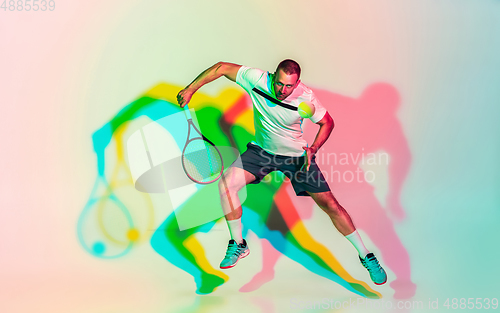 Image of Caucasian male professional sportsman playing tennis on studio background in neon light