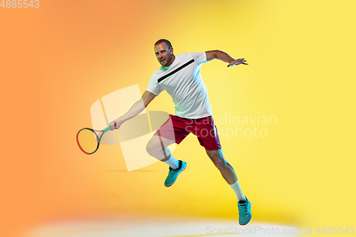 Image of Caucasian male professional sportsman playing tennis on studio background in neon light