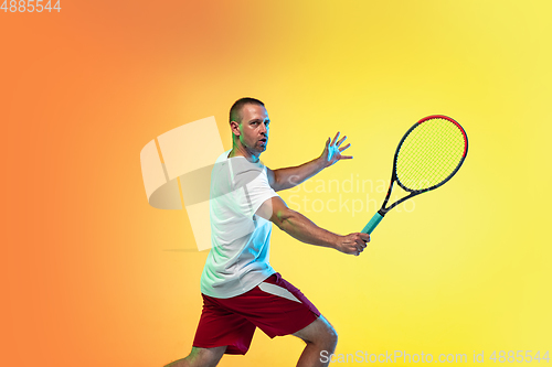 Image of Caucasian male professional sportsman playing tennis on studio background in neon light