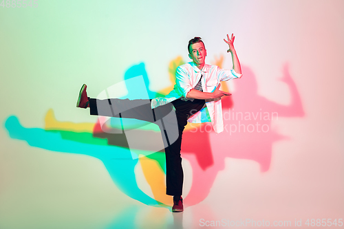 Image of Young beautiful man dancing hip-hop, street style isolated on studio background in neon light