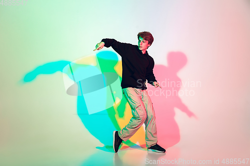 Image of Young beautiful man dancing hip-hop, street style isolated on studio background in neon light