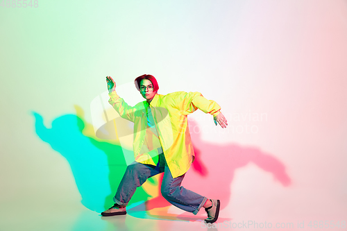 Image of Young beautiful woman dancing hip-hop, street style isolated on studio background in neon light