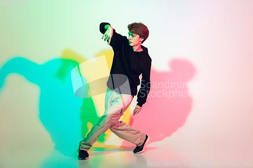 Image of Young beautiful man dancing hip-hop, street style isolated on studio background in neon light