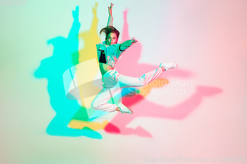 Image of Young beautiful woman dancing hip-hop, street style isolated on studio background in neon light