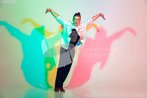 Image of Young beautiful man dancing hip-hop, street style isolated on studio background in neon light