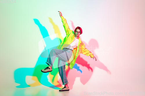 Image of Young beautiful woman dancing hip-hop, street style isolated on studio background in neon light