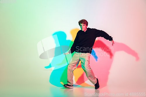 Image of Young beautiful man dancing hip-hop, street style isolated on studio background in neon light