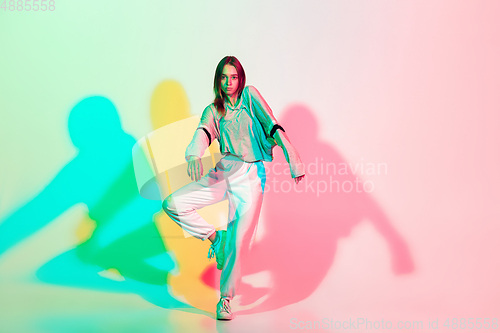 Image of Young beautiful woman dancing hip-hop, street style isolated on studio background in neon light