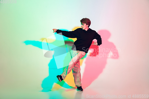 Image of Young beautiful man dancing hip-hop, street style isolated on studio background in neon light