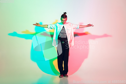 Image of Young beautiful man dancing hip-hop, street style isolated on studio background in neon light