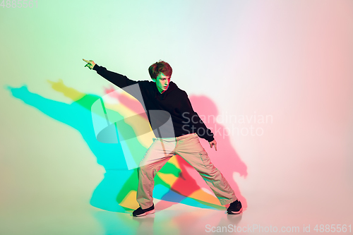 Image of Young beautiful man dancing hip-hop, street style isolated on studio background in neon light