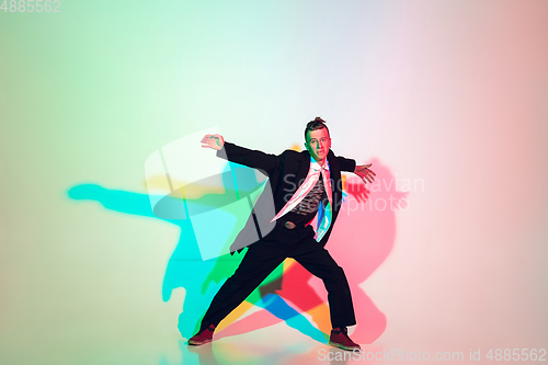 Image of Young beautiful man dancing hip-hop, street style isolated on studio background in neon light