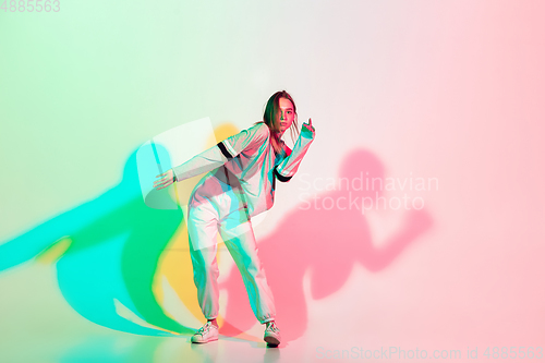 Image of Young beautiful woman dancing hip-hop, street style isolated on studio background in neon light