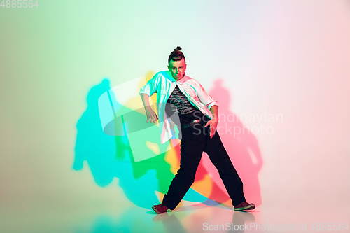 Image of Young beautiful man dancing hip-hop, street style isolated on studio background in neon light