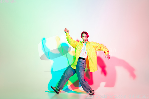 Image of Young beautiful woman dancing hip-hop, street style isolated on studio background in neon light