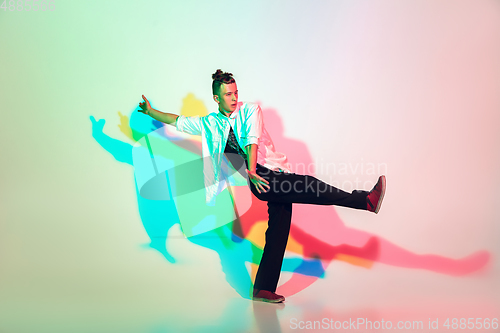 Image of Young beautiful man dancing hip-hop, street style isolated on studio background in neon light