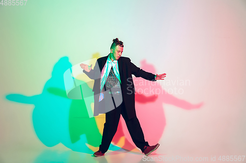 Image of Young beautiful man dancing hip-hop, street style isolated on studio background in neon light