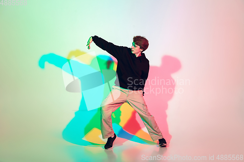 Image of Young beautiful man dancing hip-hop, street style isolated on studio background in neon light