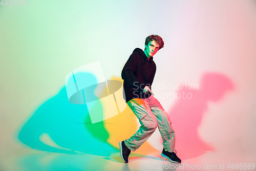 Image of Young beautiful man dancing hip-hop, street style isolated on studio background in neon light