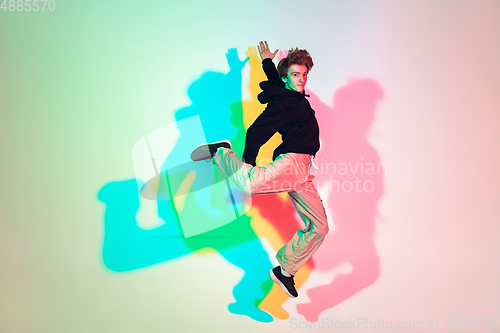 Image of Young beautiful man dancing hip-hop, street style isolated on studio background in neon light