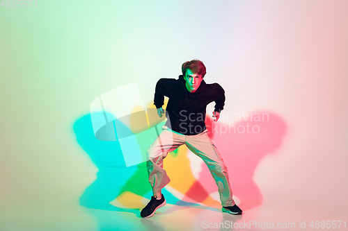 Image of Young beautiful man dancing hip-hop, street style isolated on studio background in neon light