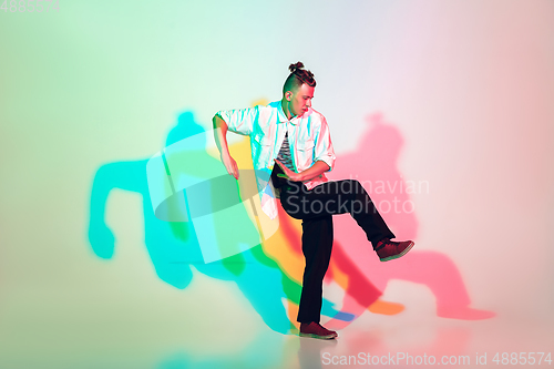 Image of Young beautiful man dancing hip-hop, street style isolated on studio background in neon light