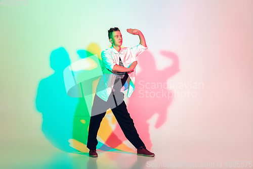 Image of Young beautiful man dancing hip-hop, street style isolated on studio background in neon light