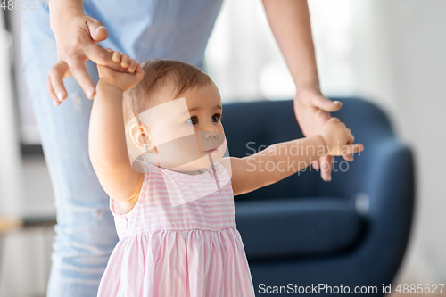 Image of baby girl learning to walk with mother's help