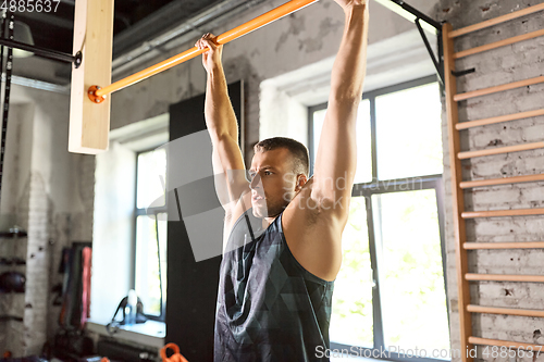 Image of man exercising on bar and doing pull-ups in gym