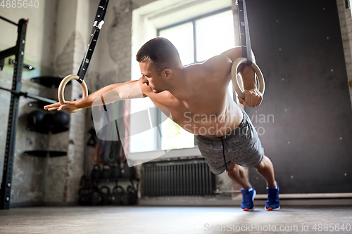 Image of man doing exercising on gymnastic rings in gym