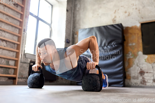 Image of young man doing kettlebell push-ups in gym