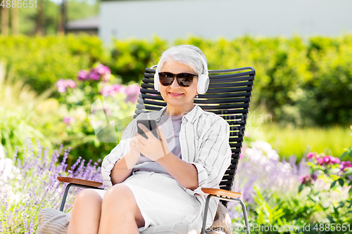Image of old woman with headphones and smartphone at garden