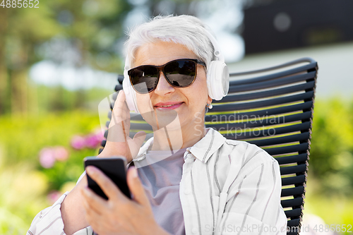 Image of old woman with headphones and smartphone at garden