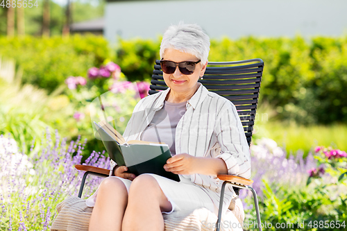 Image of happy senior woman reading book at summer garden