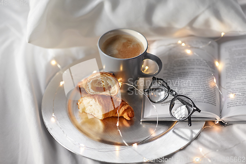 Image of croissants, cup of coffee, book and glasses in bed