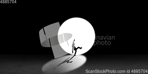 Image of Silhouette of man walking in the night toward the light, view from above