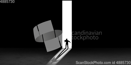 Image of Silhouette of man walking in the night toward the light, view from above