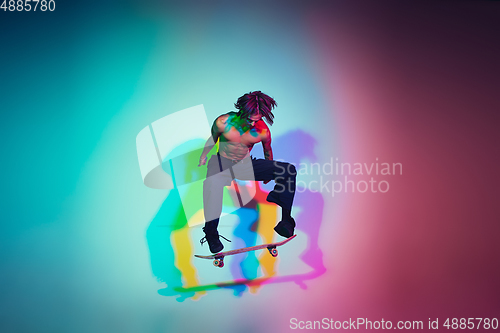 Image of Skateboarder doing a trick isolated on studio background in colorful neon light