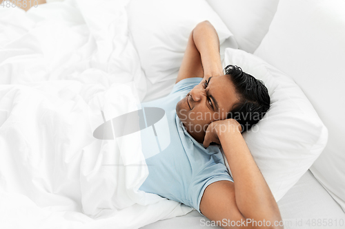 Image of annoyed indian man lying in bed and closing ears